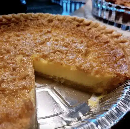A sliced southern chess pie served with a dollop of whipped cream on a wooden table