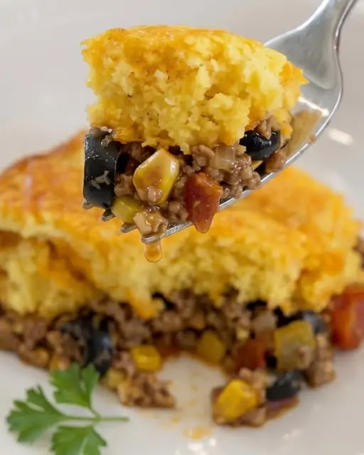 A slice of tamale pie served with sour cream and cilantro.