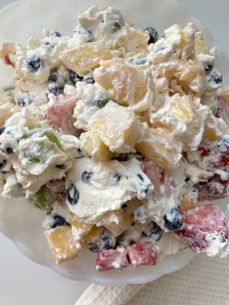 A large serving bowl filled with creamy cheesecake fruit salad garnished with mint