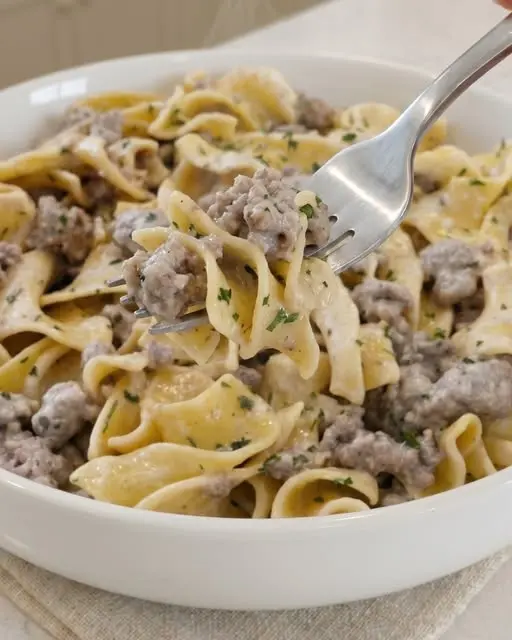 A bowl of beef and ranch noodles served with a side of steamed green beans