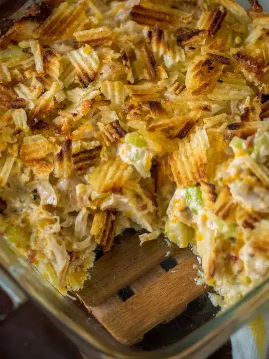 A serving of crispy chicken salad casserole on a white plate with a side of greens