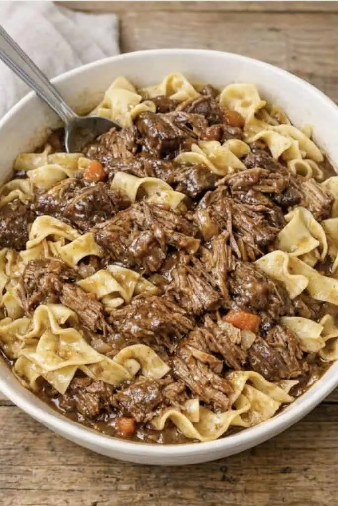 A white bowl filled with beef and noodles, topped with a sprig of fresh parsley.