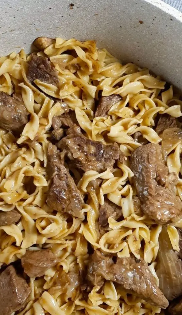 Finished crockpot beef tips served over wide egg noodles in a white bowl