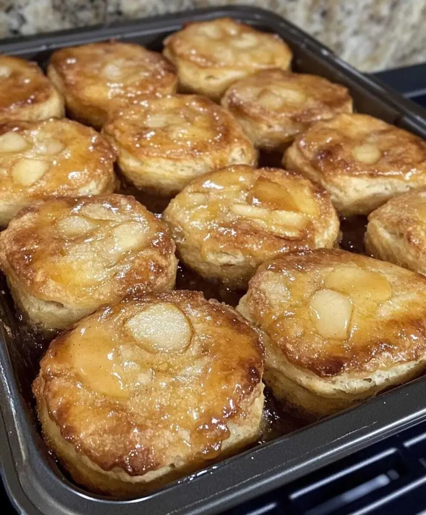 Freshly baked apple pie biscuits drizzled with white glaze on a cooling rack.