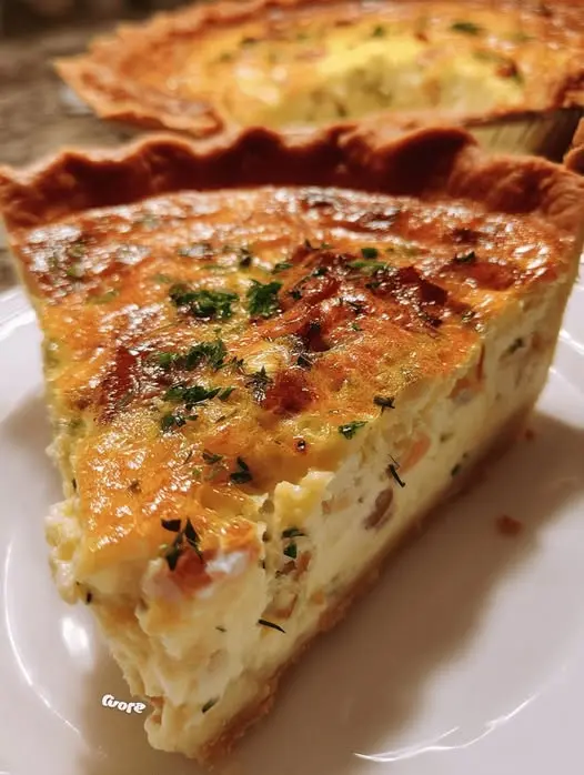 A slice of bacon and cheese quiche served on a white plate with a side salad