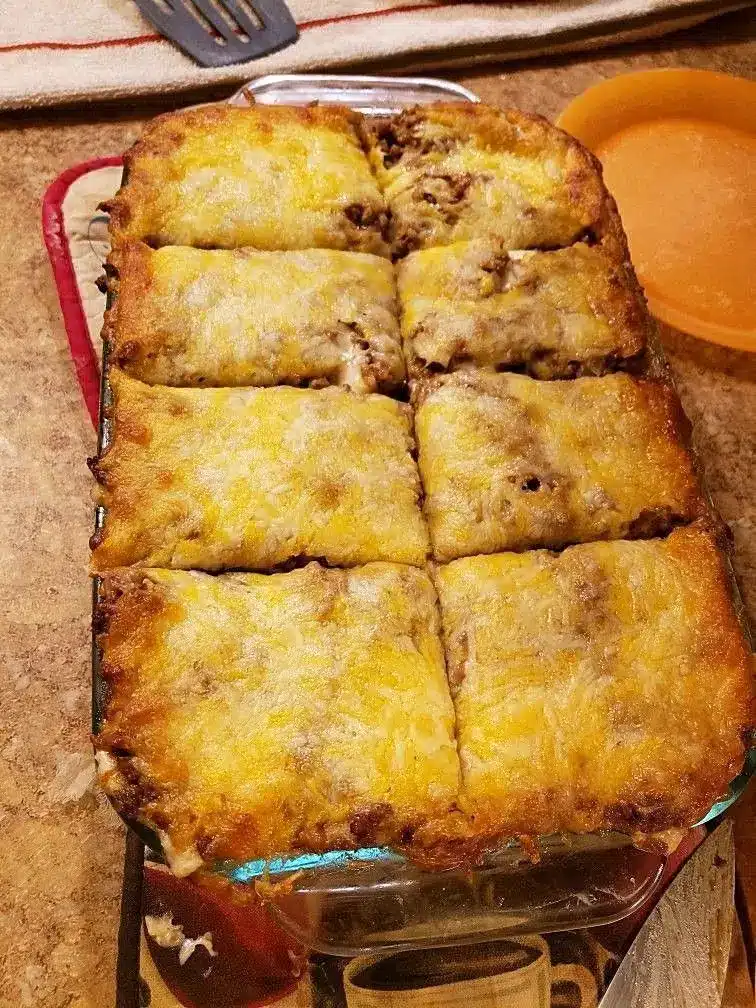 A slice of beef burrito casserole served on a white plate topped with fresh shredded lettuce, diced tomatoes, and a dollop of sour cream.