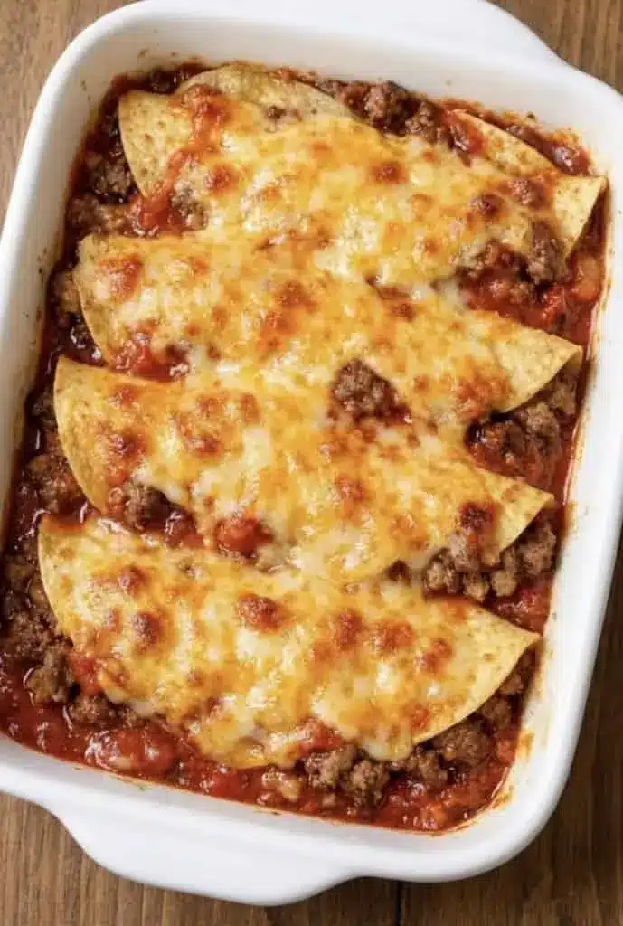 A close-up of a serving of layered beef enchilada bake on a white plate with sour cream and avocado.