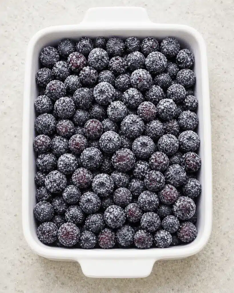A warm scoop of blueberry dump cake served in a white bowl with a melting scoop of vanilla ice cream.