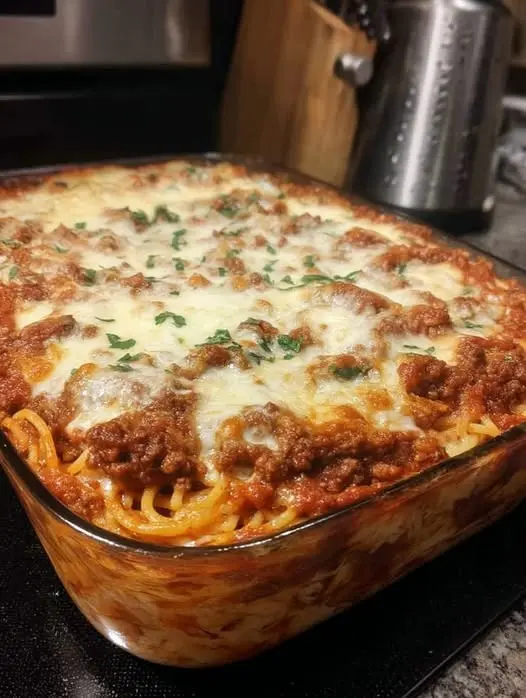 The finished baked spaghetti in a ceramic dish, featuring a golden-brown cheese crust and fresh parsley garnish.