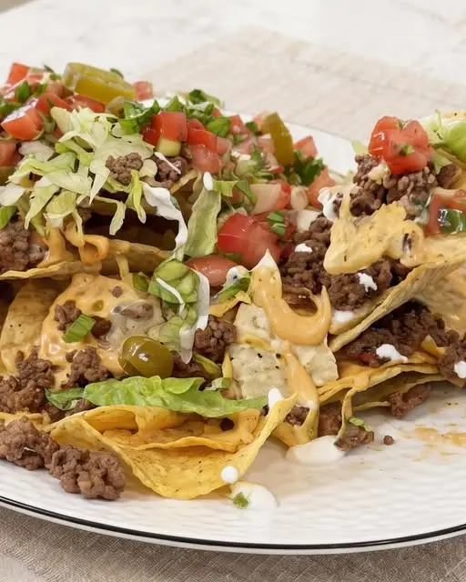 A finished tray of easy cheesy beef nachos topped with sour cream, cilantro, and fresh tomatoes.
