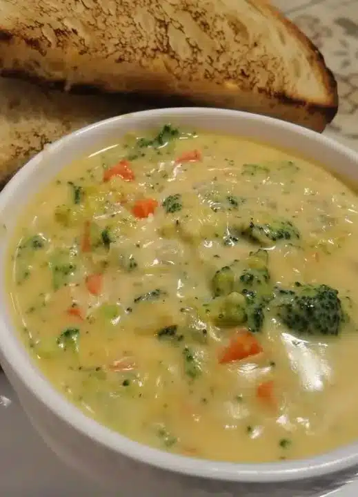 A close-up of cheesy chicken noodles being stirred in a pan, showing the thick, glossy sauce.