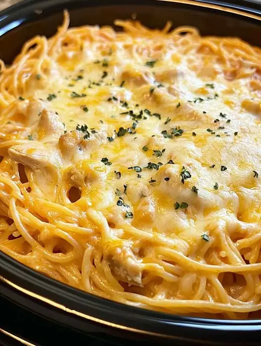 A serving of cheesy chicken spaghetti on a white plate garnished with fresh herbs