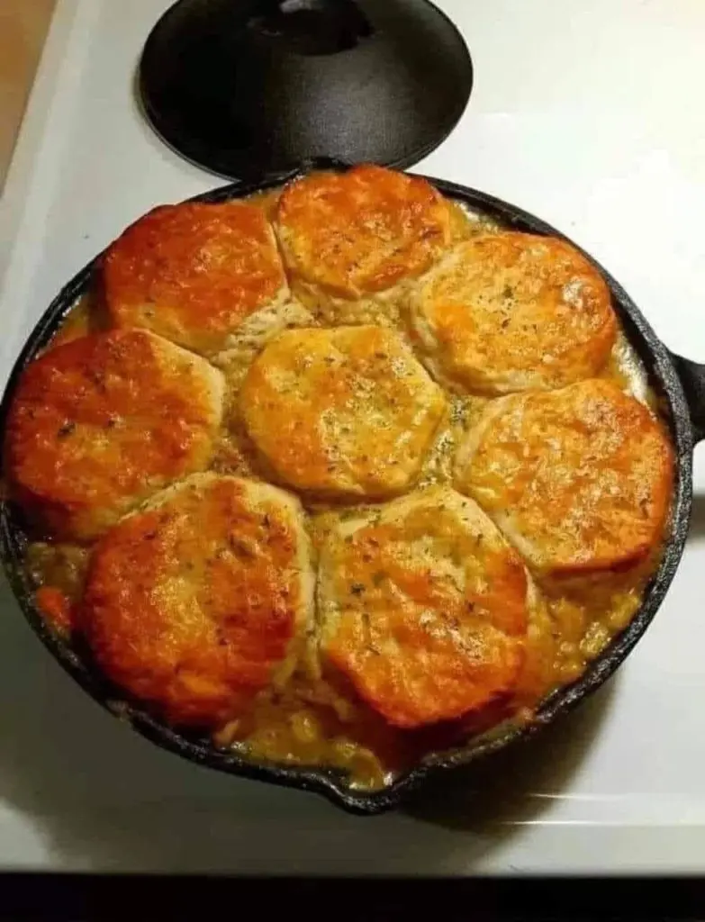 A serving of chicken pot pie with a fluffy biscuit on a white plate.