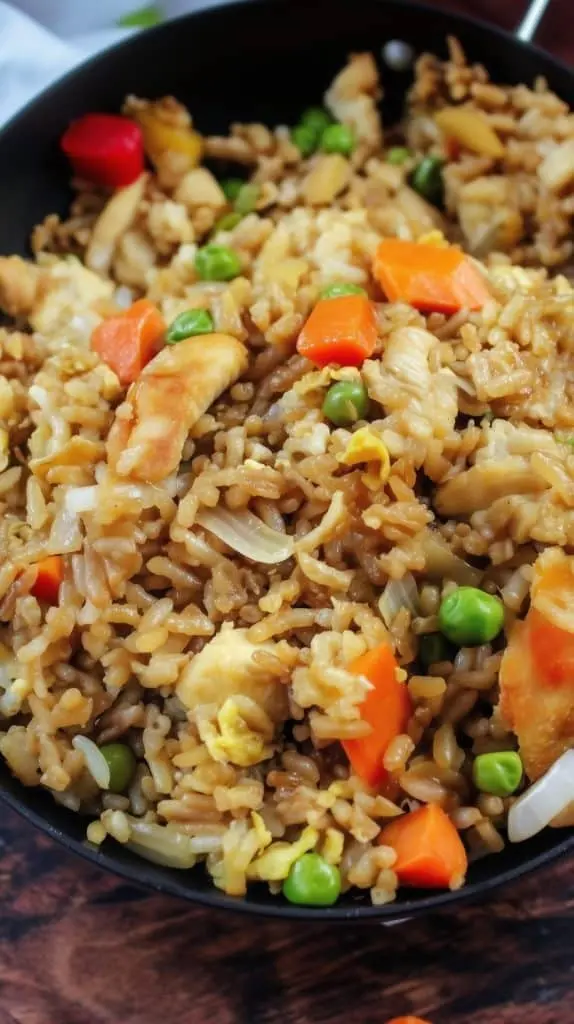 A close up of chicken fried rice served in a bowl garnished with fresh scallions and sesame seeds