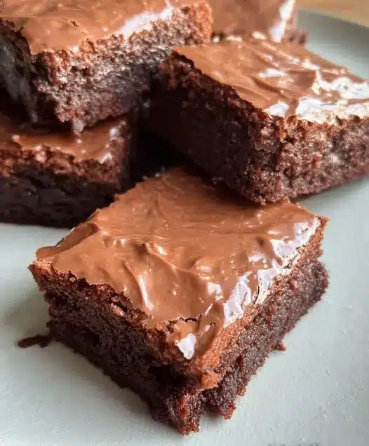 A stack of sliced chocolate frosted brownies on a cooling rack