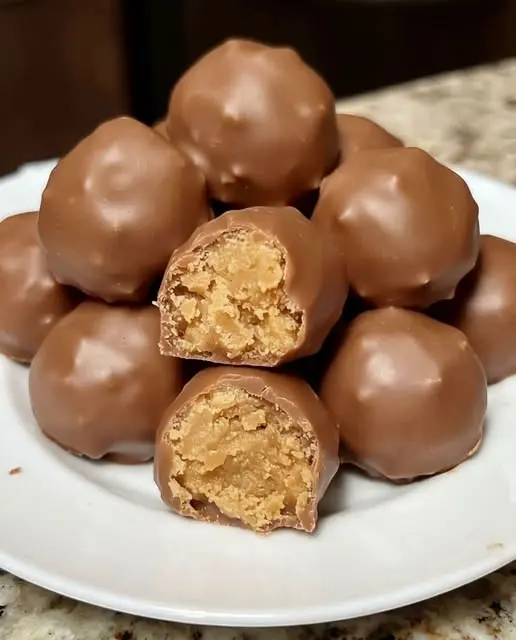 A close up of finished chocolate peanut butter balls stacked on a white plate.