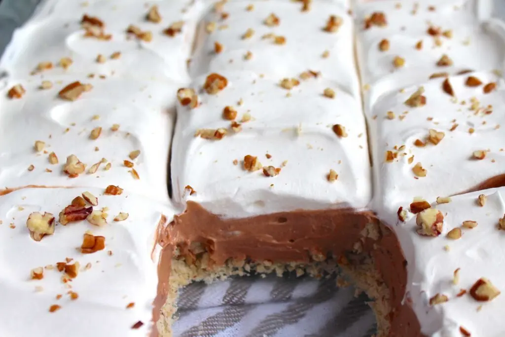 a square slice of chocolate pecan delight on a white plate showing the pecan crust and creamy layers