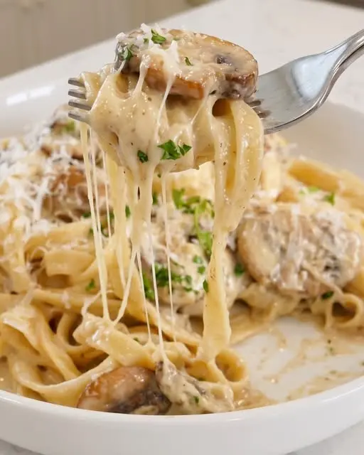 A finished plate of creamy mushroom pasta with fresh herbs and a fork