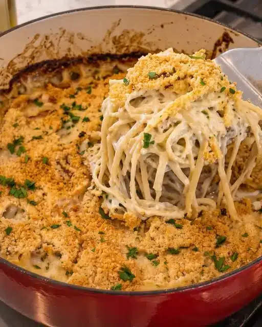 A portion of turkey tetrazzini being lifted from a baking dish, showing the creamy interior and melted cheese.