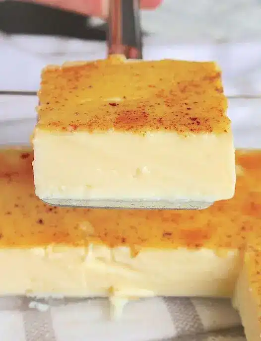 Several individual ramekins of golden-baked egg custard sitting in a water bath inside a roasting pan.