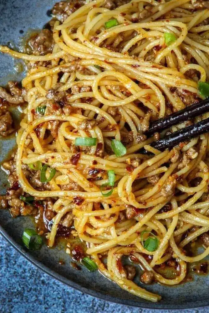 A close-up view of beef and noodles in a skillet with a wooden spoon serving a portion.