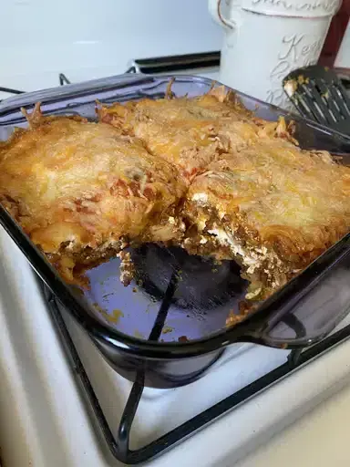 a sliced piece of ground beef taco lasagna served on a white plate with sour cream