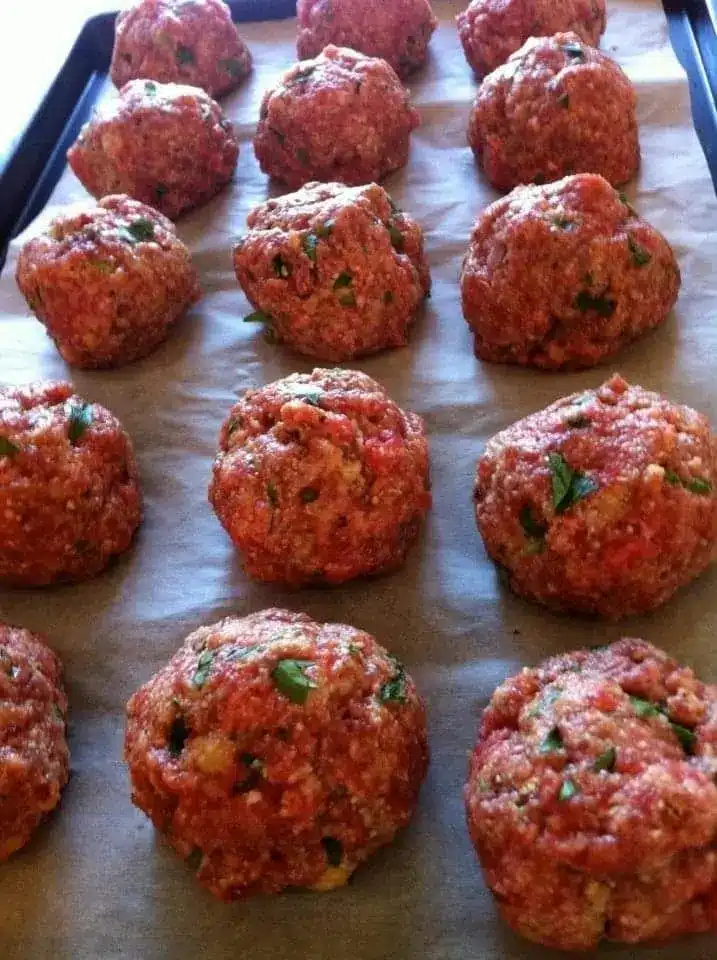Freshly baked meatballs on a baking sheet with golden brown edges and fresh parsley garnish