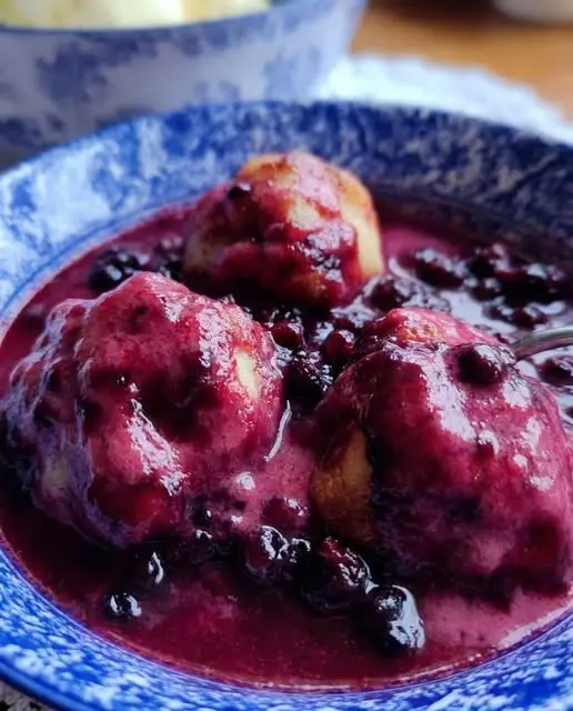 A serving of berry cobbler in a bowl topped with a melting scoop of vanilla ice cream.