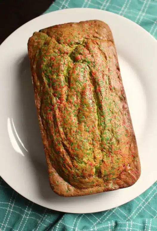 Full loaf of pistachio bread topped with crushed nuts on a white plate