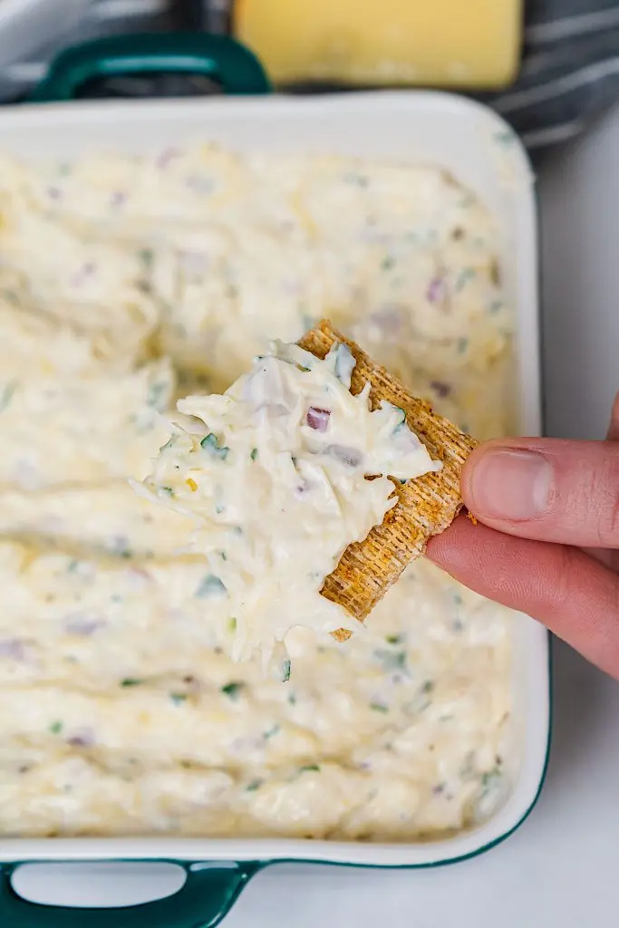 Close up of Jarlsberg cheese dip on a toasted baguette slice with a side of fresh vegetables.