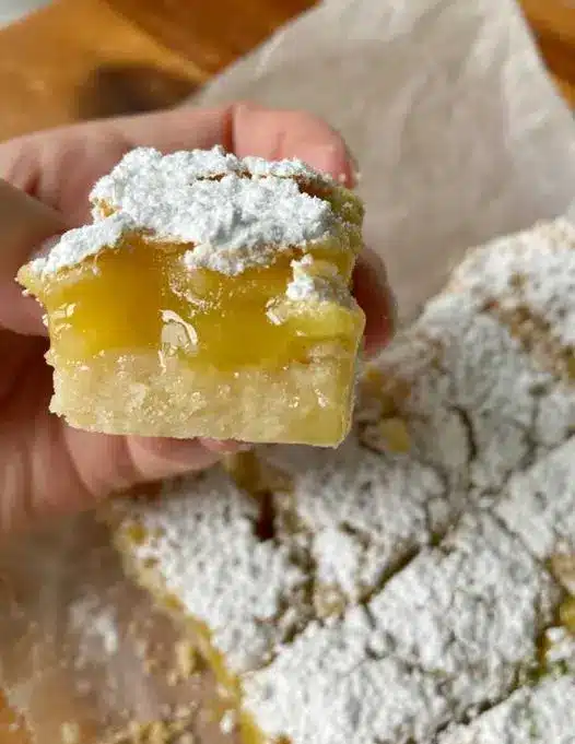Square cut lime bars on a white plate with a dusting of powdered sugar