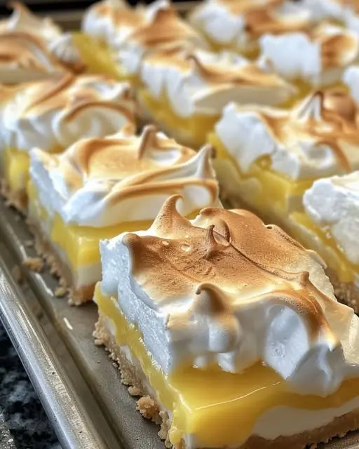 A close-up shot of a sliced lemon meringue bar showing the distinct layers of crust, curd, and meringue