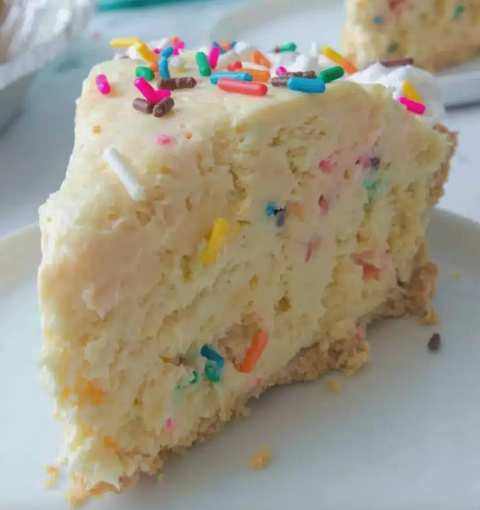 A slice of no-bake funfetti cheesecake on a plate showing the creamy texture and rainbow sprinkles