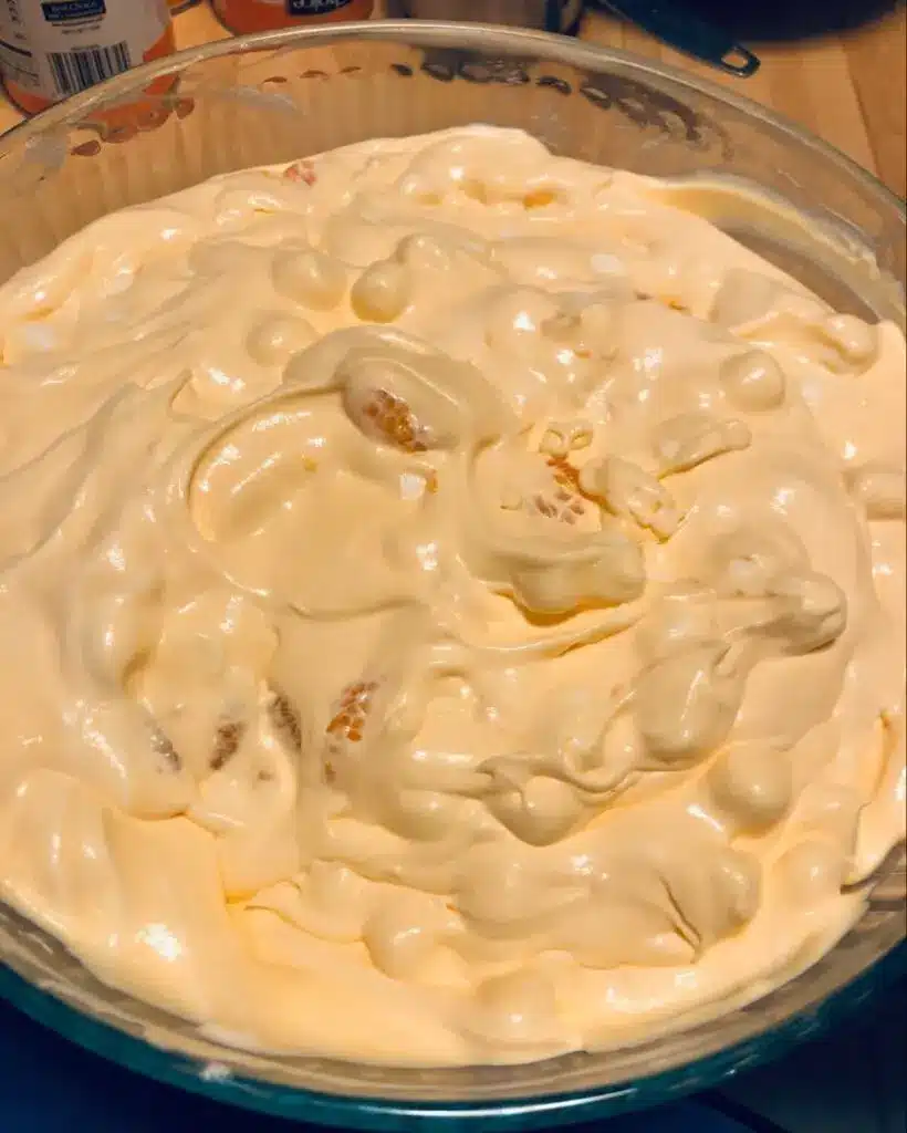 A close-up of orange creamsicle fluff in a glass serving bowl garnished with a mint leaf.