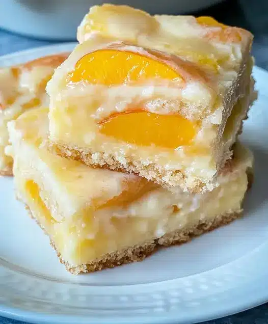 A close-up of a sliced peach cream cheese bar showing the creamy fruit layers