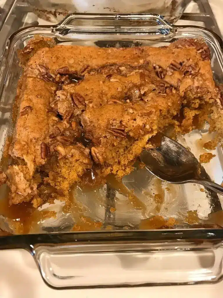 A serving of pumpkin pecan cobbler on a white plate with a scoop of melting vanilla ice cream