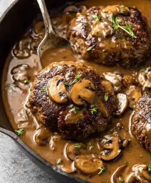 A single Salisbury steak patty served with mashed potatoes and gravy on a white plate.