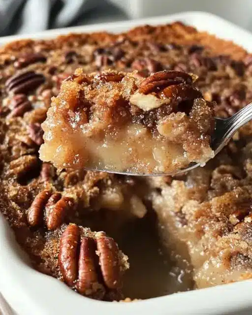 A serving of pecan cobbler in a bowl topped with a scoop of melting vanilla ice cream.