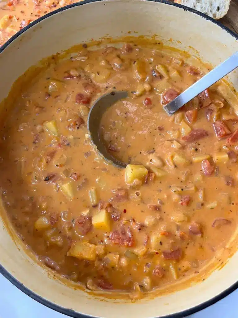 A close up of fire roasted tomato soup in a pot being stirred with a wooden spoon