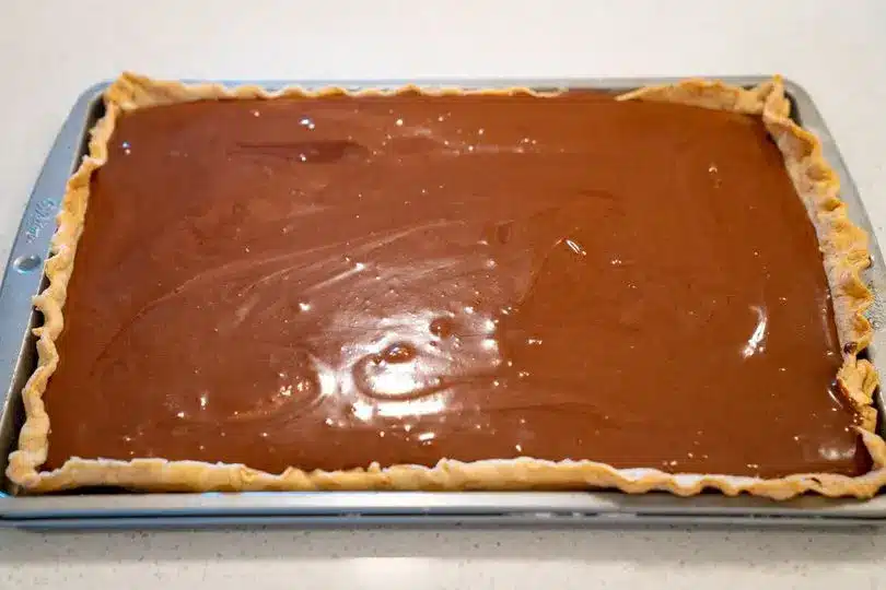 A close up of a slice of french silk slab pie showing the layers of crust, chocolate mousse, and cream