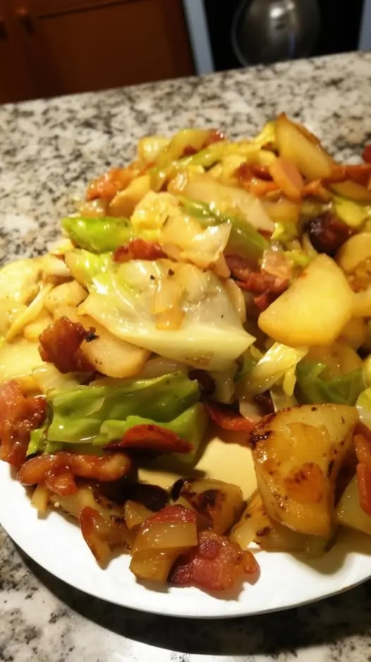 A close-up of served fried cabbage and potatoes on a plate, garnished with fresh herbs.