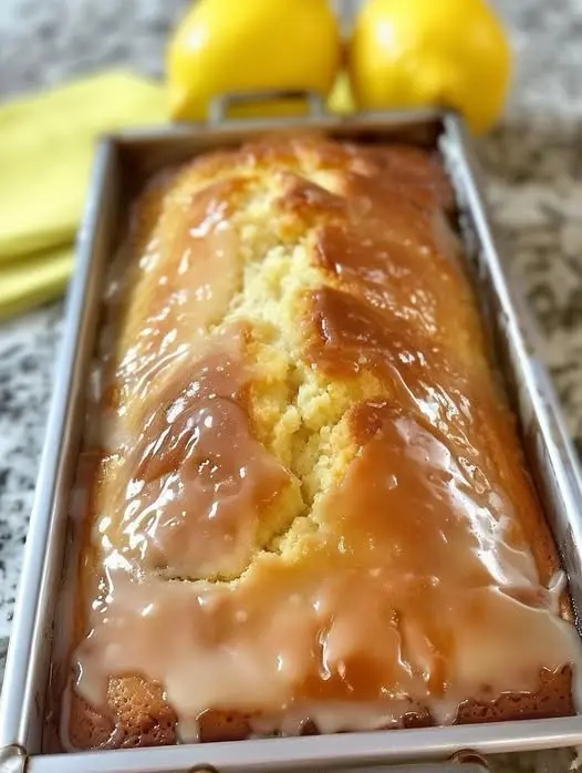 A close-up slice of moist lemon pound cake with a thick white glaze dripping down the side.