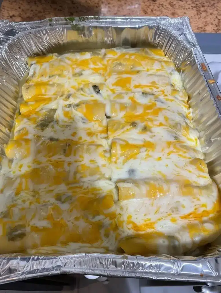 A tray of green chili chicken enchiladas served with lime wedges and fresh cilantro