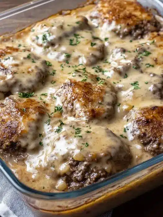 Plated hamburger steak with a side of mashed potatoes and green beans, topped with plenty of mushroom gravy.