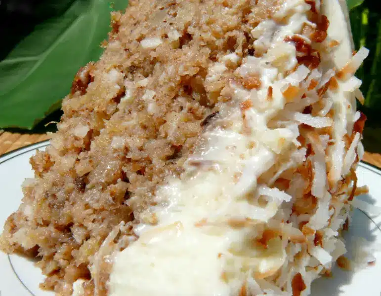 A whole Hawaiian wedding cake in a baking dish, topped with whipped cream, nuts, and coconut