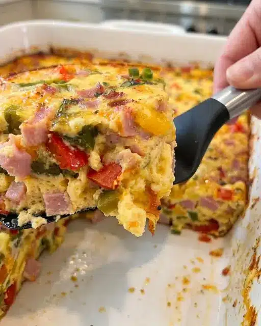 A sliced portion of a savory morning dish on a plate, showing the layers of egg and vegetables.