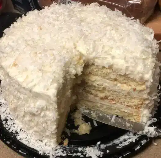 A slice of coconut layer cake on a plate showing the moist interior and white frosting.