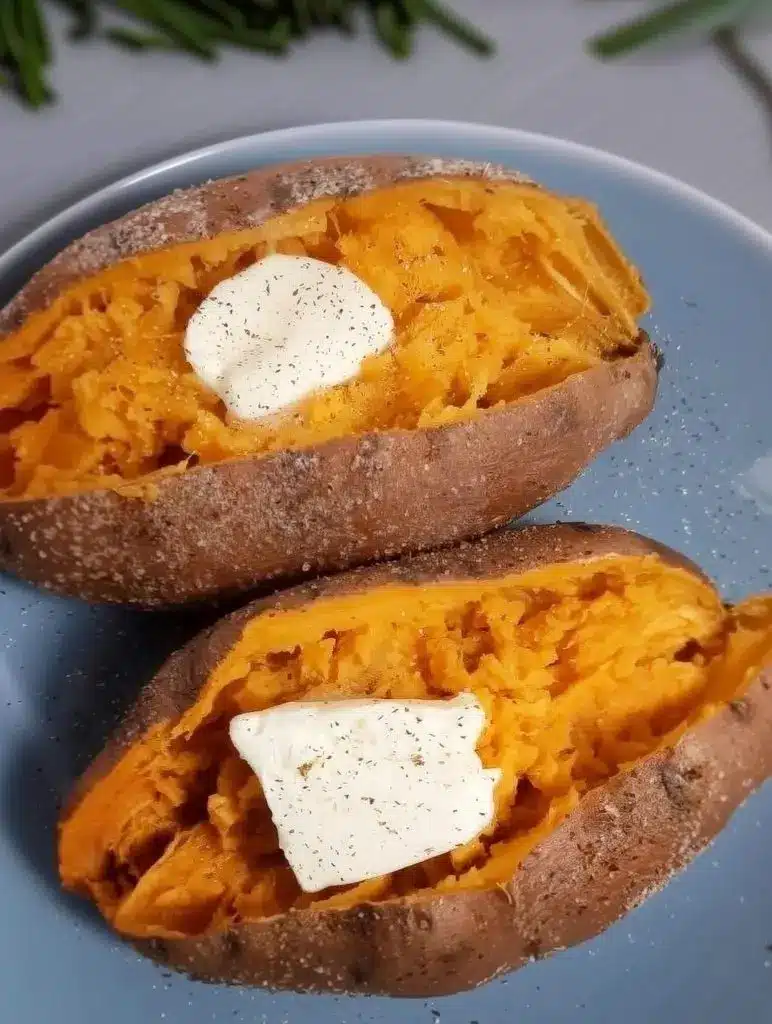 A perfectly cooked, steaming microwaved sweet potato sliced open and topped with a pat of melting butter.
