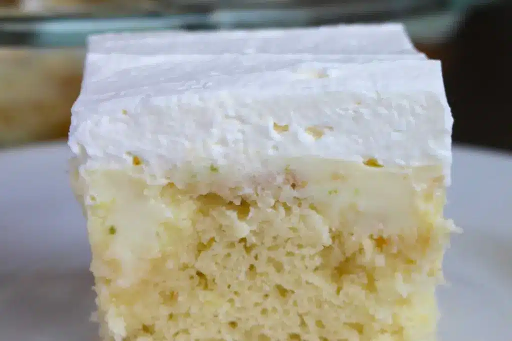 A slice of key lime poke cake on a plate garnished with a lime slice and graham cracker crumbs