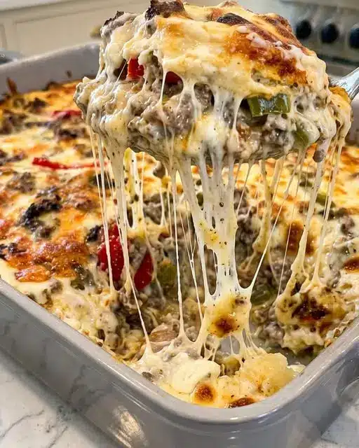 A whole baking dish of philly cheesesteak lasagna with a golden brown cheese topping and visible bits of green pepper.